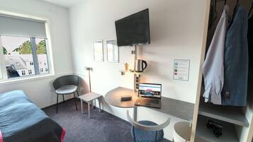 Habitación de hotel con cama, escritorio con una computadora portátil, una silla, televisor montado en la pared y un armario.