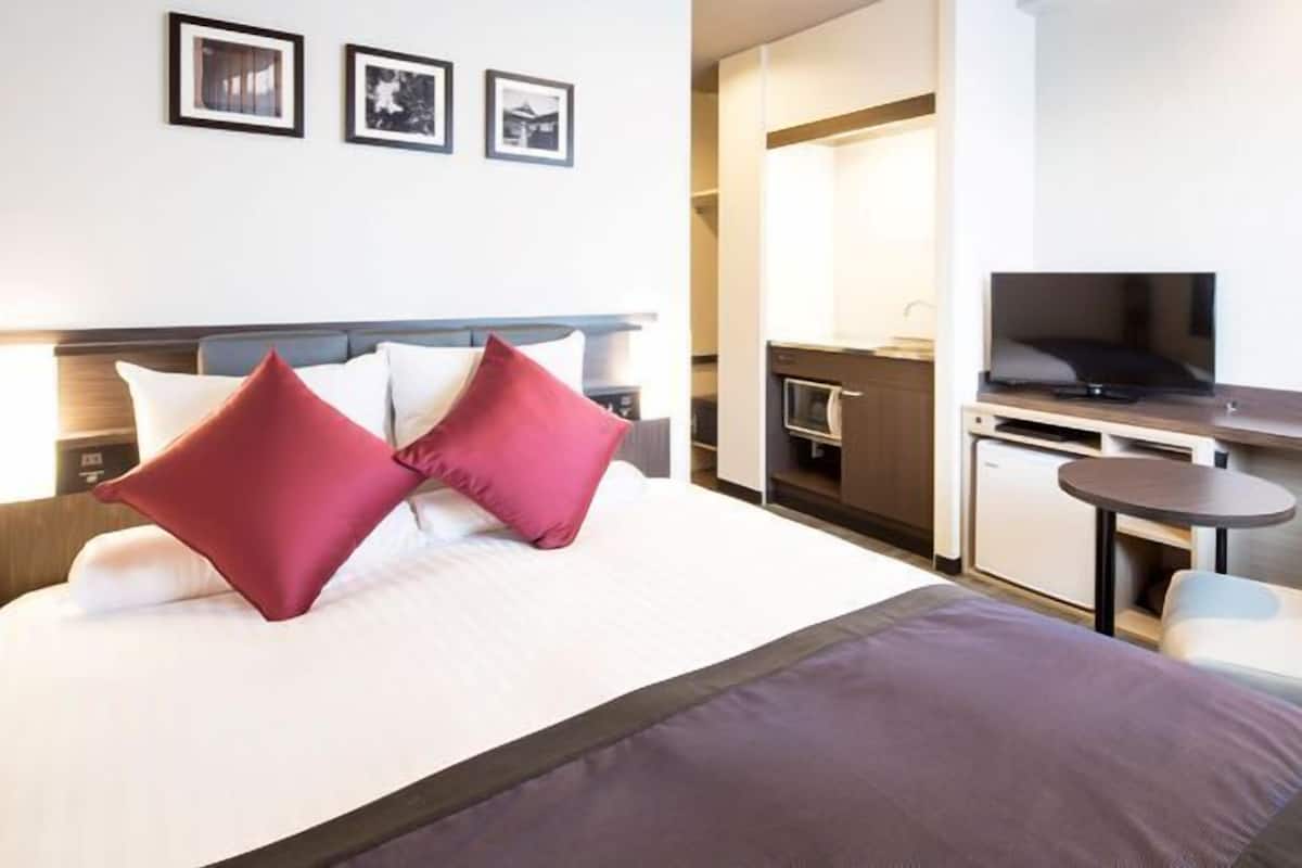 Ein Hotelzimmer mit Bett, Fernseher, einer kleinen Küchenzeile und einer Sitzecke mit Tisch und Stühlen.