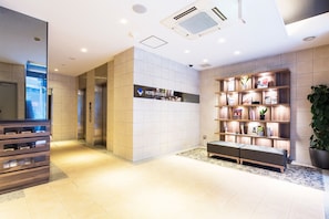 A modern hotel lobby with a reception desk, a seating area, and a wall-mounted information board.
