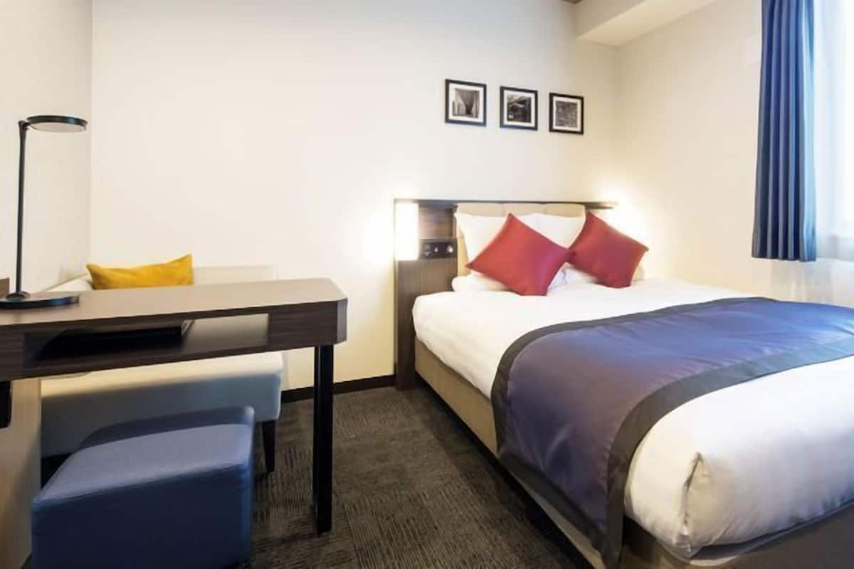 Ein Hotelzimmer mit Bett, Schreibtisch, Stuhl und Nachttisch.