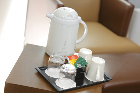 A tray with a white electric kettle, two glass cups, a tea sachet, and two white mugs on a wooden table.