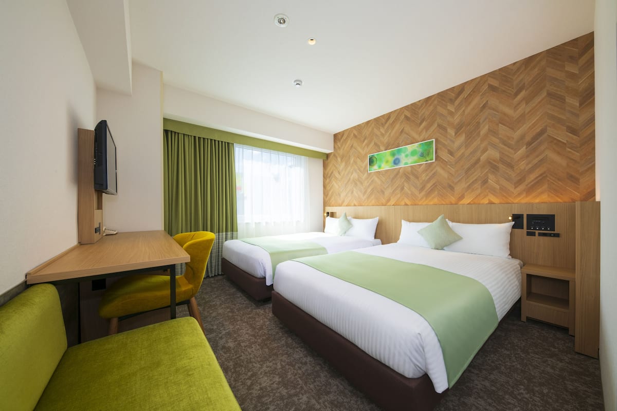Une chambre d’hôtel avec deux lits, un bureau, une chaise et un téléviseur.