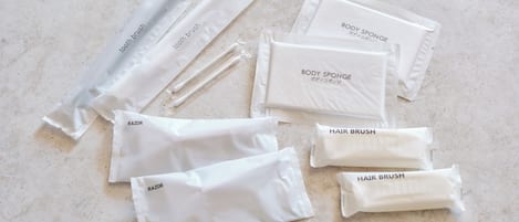 A collection of white personal care items, including body sponge, razor, and hair brush, arranged on a marble surface.