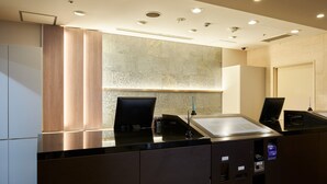 Ein modernes Badezimmer mit einem großen Spiegel, einem Waschbecken und einer Toilette. Es gibt Schränke mit dunkler Furnierung und eine heller Wand im Hintergrund.