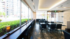 Eine moderne Hotelhalle mit einer langen Rezeption, einer Sitzecke und großen Fenstern mit Blick auf die Stadt.