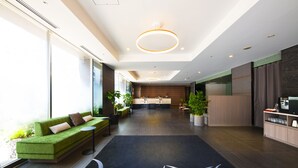 A modern hotel lobby with a green sofa, a reception desk, a kitchen area, and a large window providing natural light. - Hotel Villa Fontaine Tokyo - Kudanshita (Tokyo)