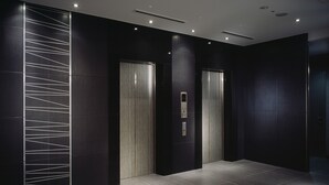 A modern elevator with a digital display, a wall with a geometric light design, and a dark floor. - Hotel Villa Fontaine Tokyo - Kudanshita (Tokyo)
