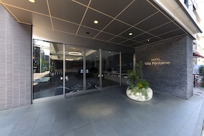 The entrance of HOTEL Villa Fontaine with a modern design, featuring a glass facade, a stone wall with the hotel name, and a potted plant. - Hotel Villa Fontaine Tokyo - Kudanshita (Tokyo)
