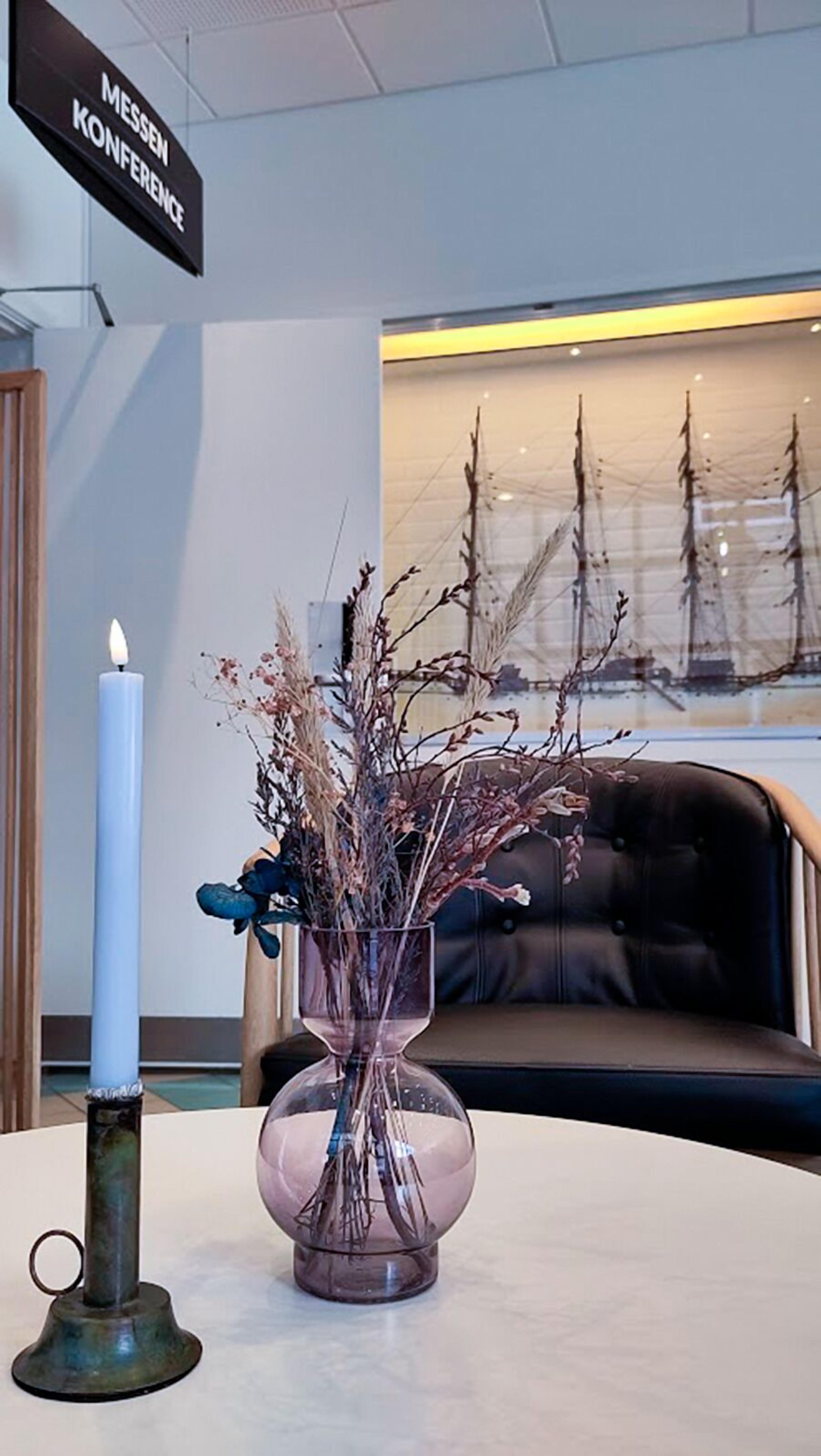 A table with a lit candle, a glass vase with dried branches, and a sign reading "MESSEN CONFERENCE".
