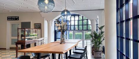 A spacious room with a wooden table and black chairs, large windows, and a ceiling with recessed lighting.