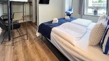 Une chambre d’hôtel avec un lit superposé, un bureau, une chaise, une télévision et une fenêtre donnant sur des immeubles.