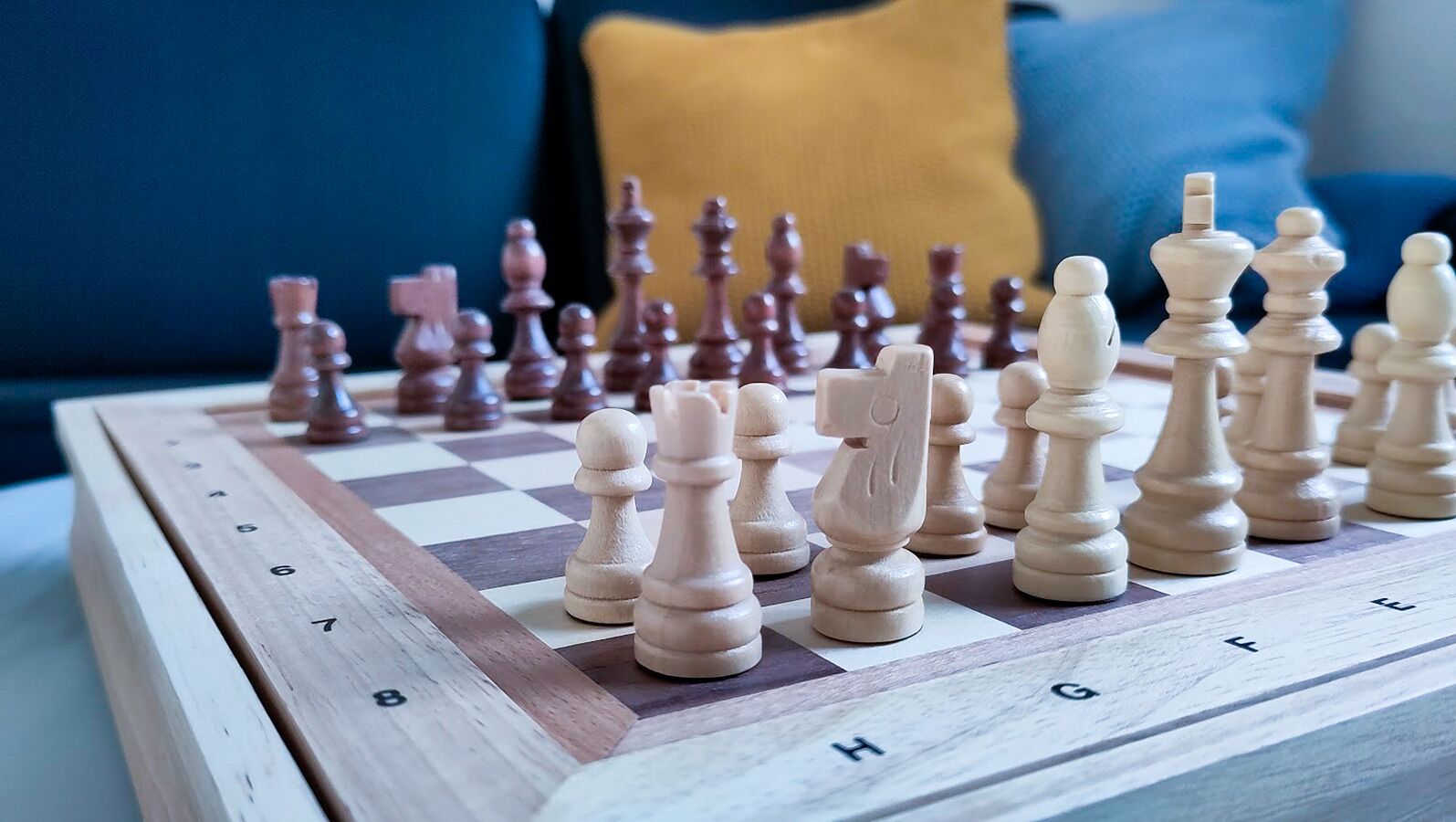 A chessboard with pieces on a wooden table, set against a blue and yellow background.