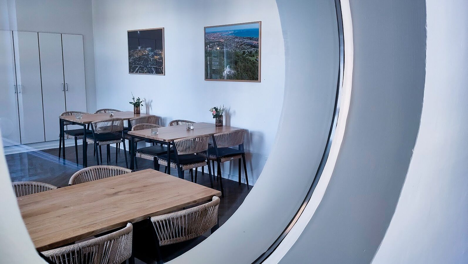 A conference room with a large table and chairs, two framed pictures on the wall, and a view of a cityscape through a window.