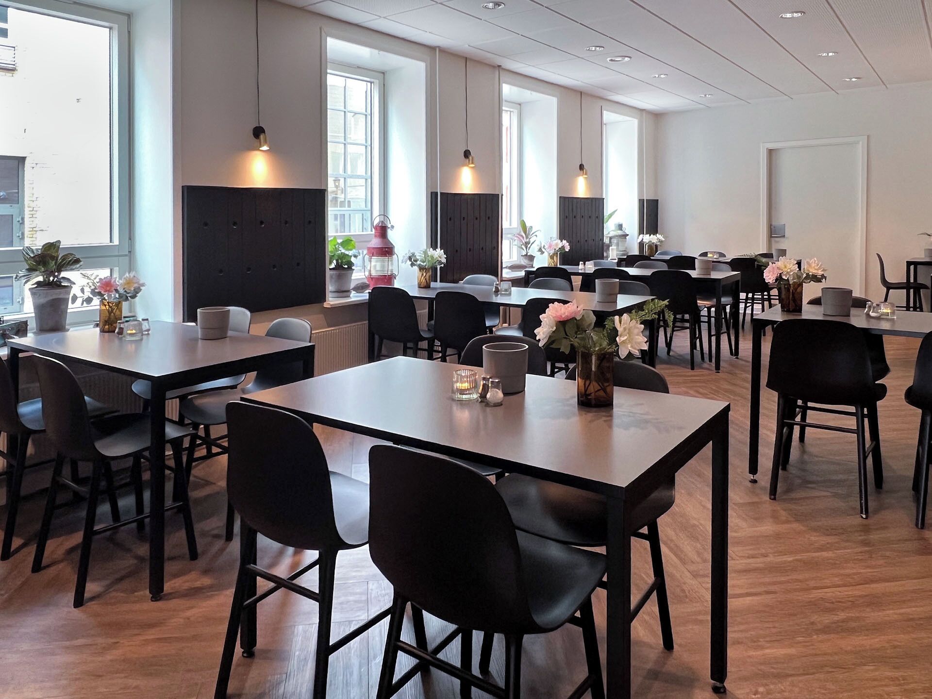 A spacious dining area with multiple tables and chairs, large windows, and potted plants.