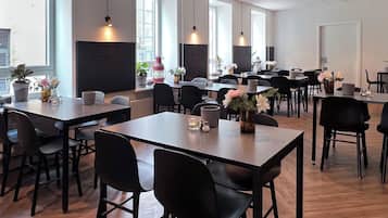 A spacious dining area with multiple tables and chairs, large windows, and potted plants.