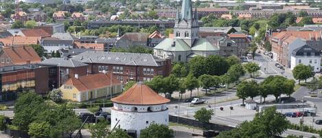 Un paysage urbain caractérisé par un clocher d’église imposant, une tour ronde et un mélange de bâtiments résidentiels et commerciaux.