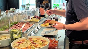 Un bufé con diversas opciones de comida, incluyendo un tazón grande de sopa, pepinos en rodajas y diferentes tipos de carne.