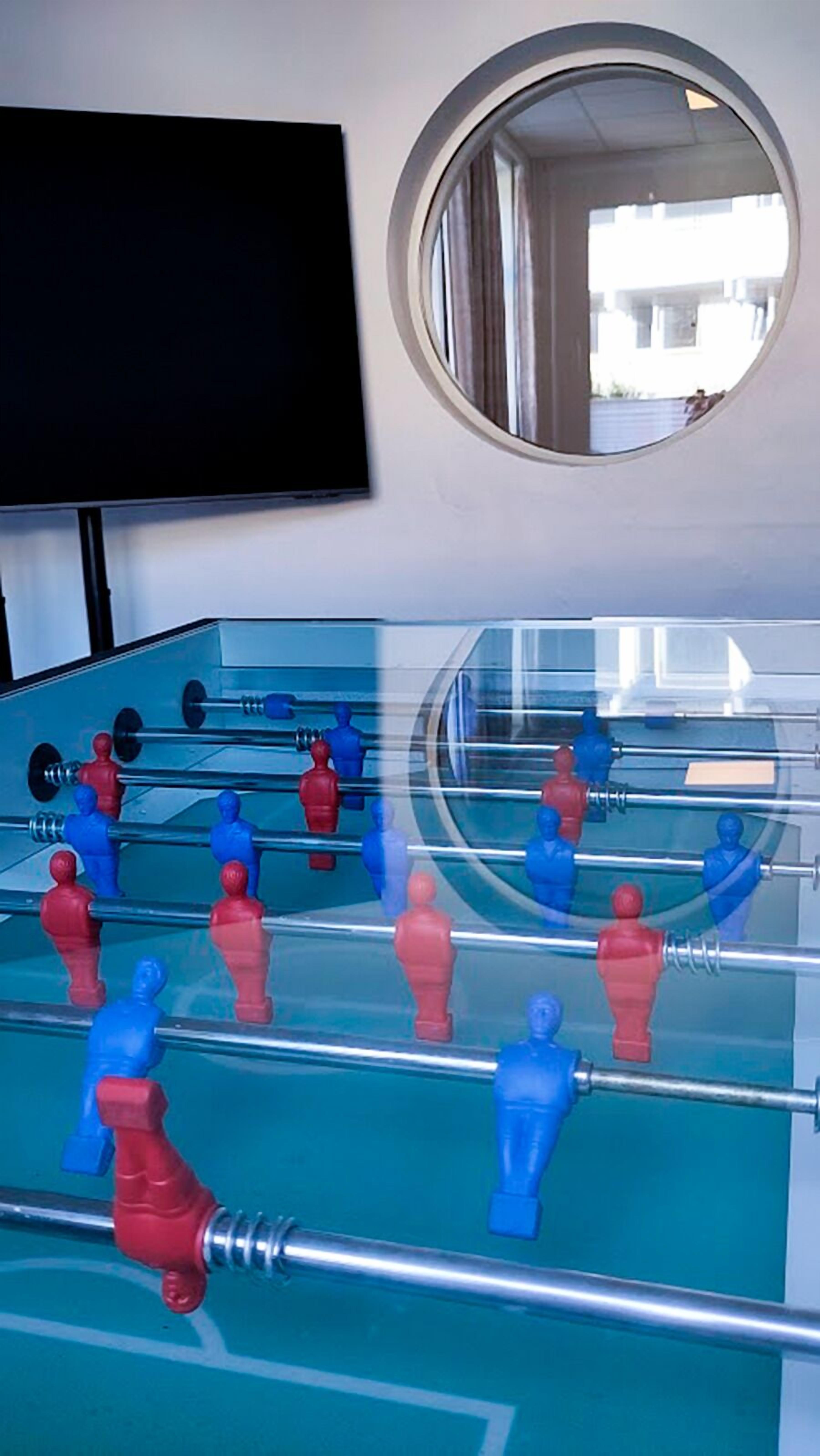 A foosball table in a room with a TV mounted on the wall and a round mirror.