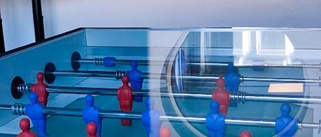A foosball table in a room with a TV mounted on the wall and a round mirror.