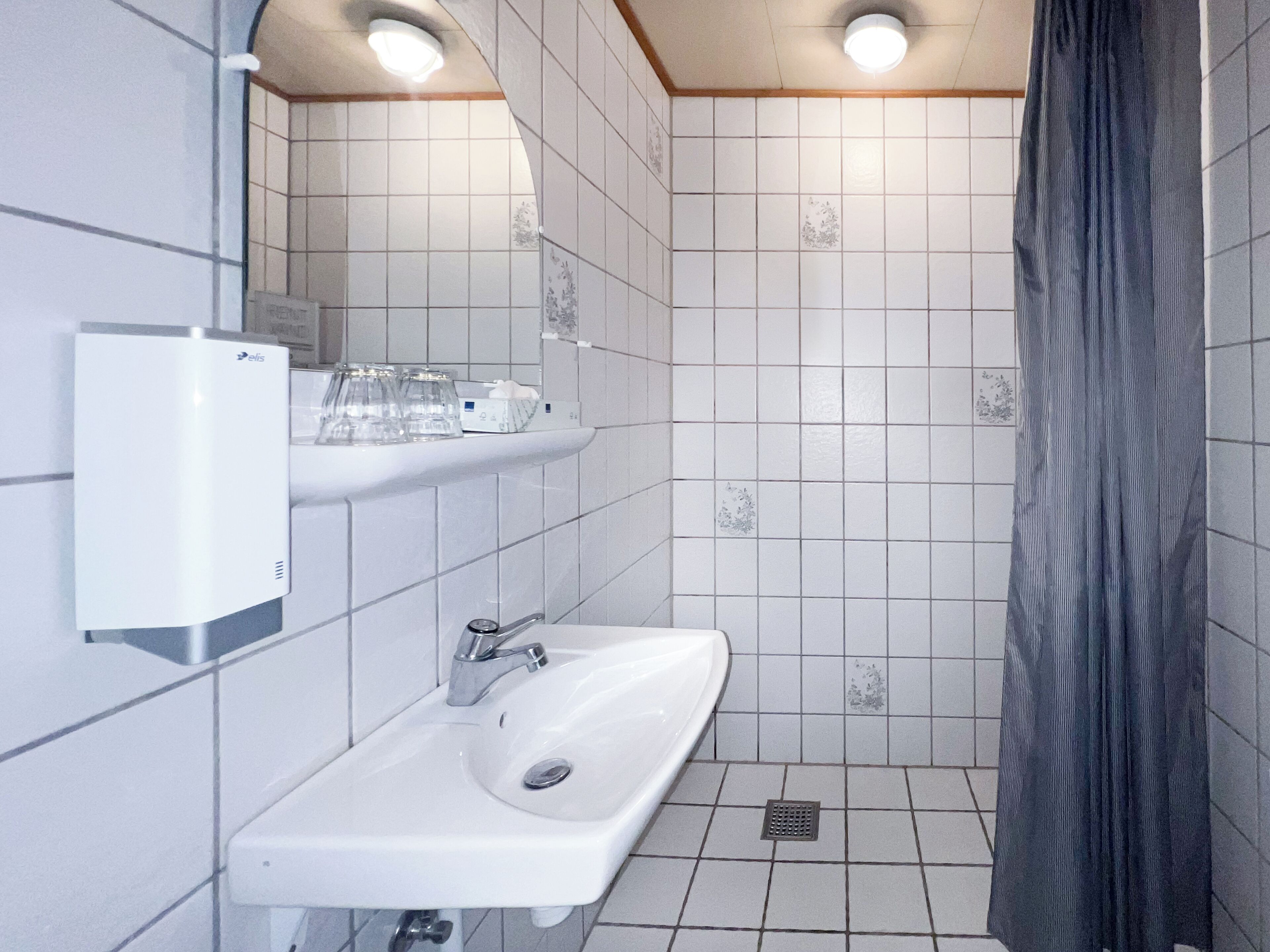 Un bagno con lavandino bianco, specchio e tenda per la doccia.