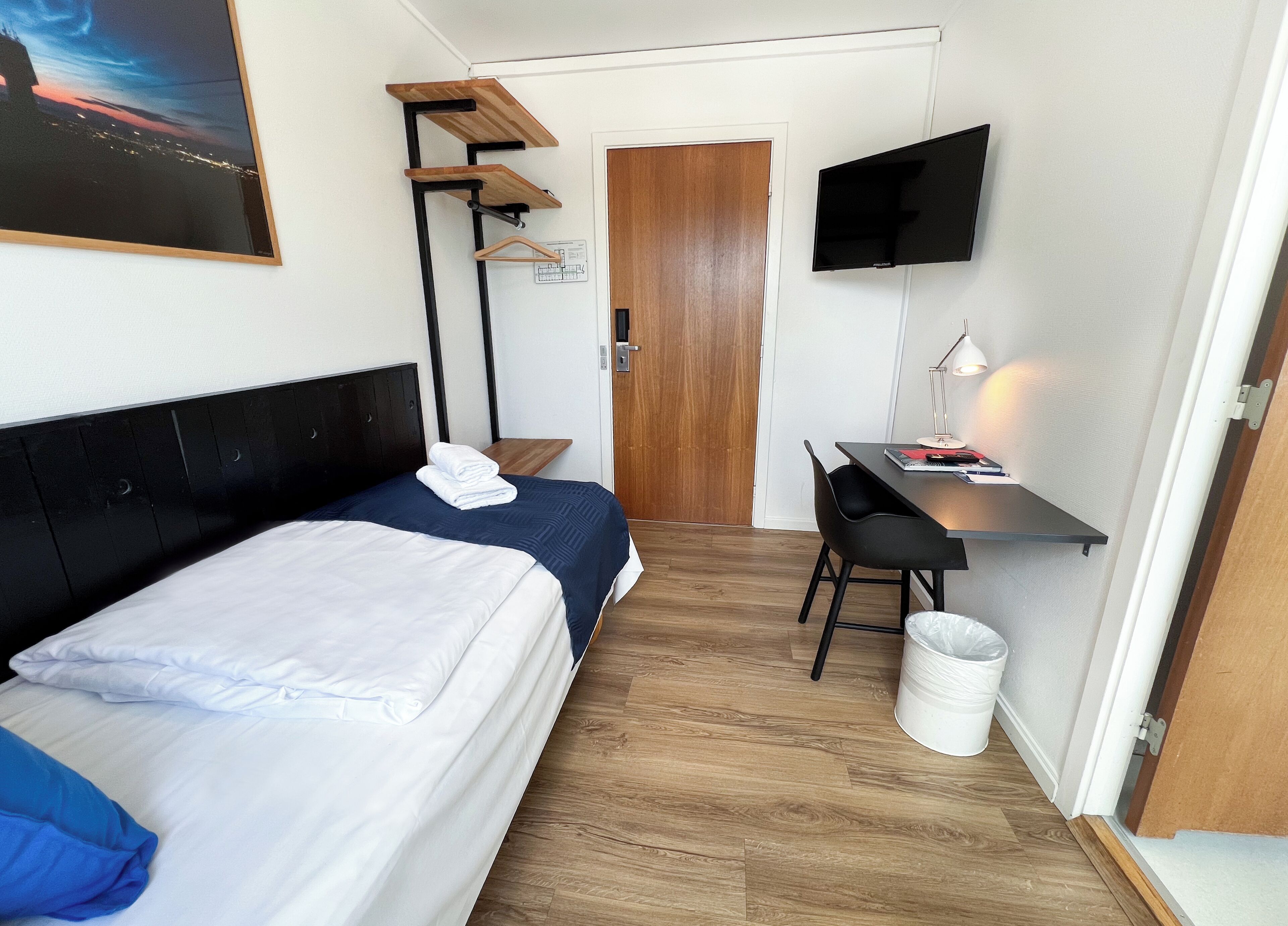 Quarto de hotel com duas camas, uma escrivaninha, uma televisão e um quadro na parede.