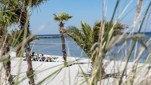 Una playa con palmeras y una vista despejada del océano. Hay sillas de descanso y un voleibol en la arena.