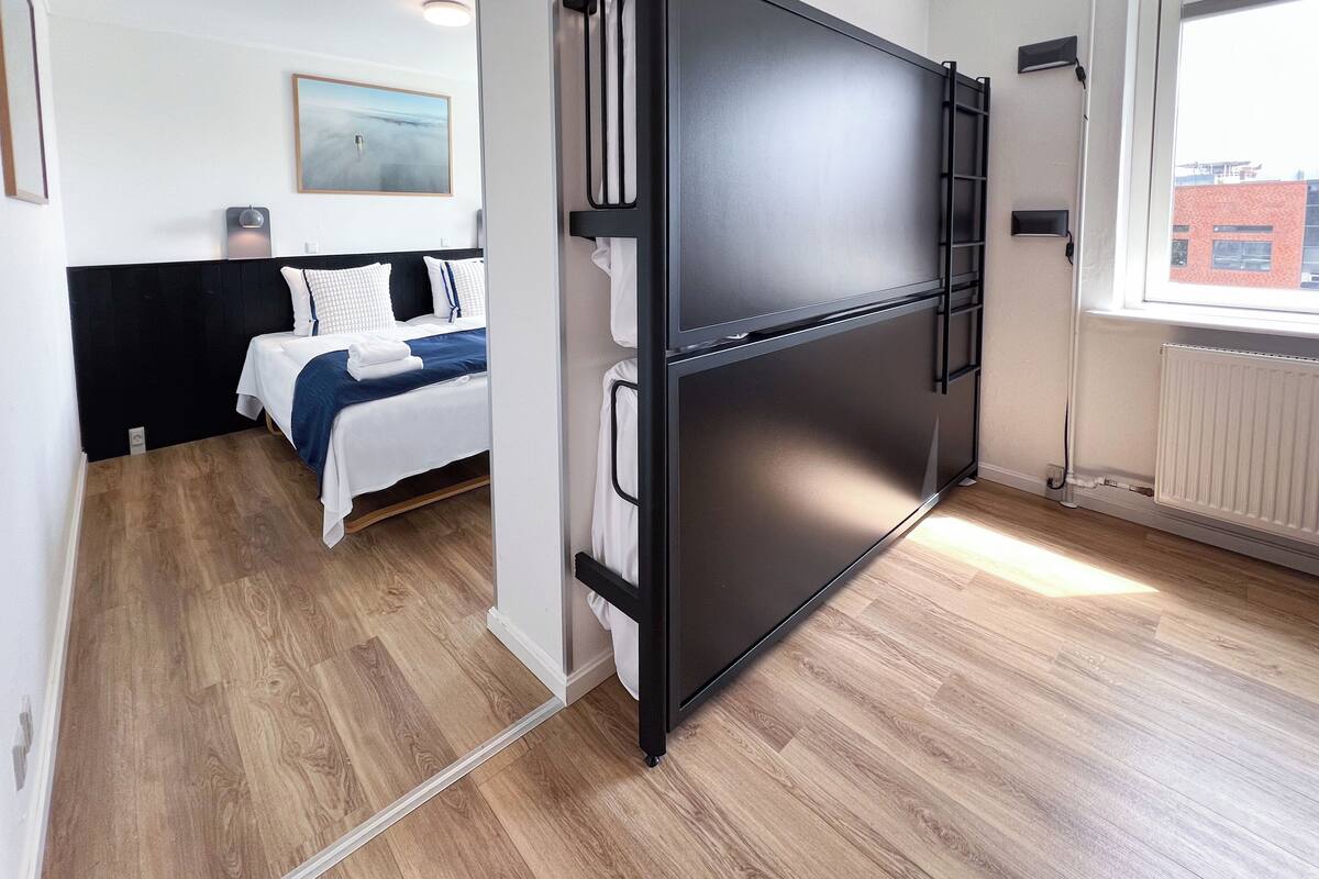 Quarto de hotel moderno com cama, guarda-roupa preto e vista para um edifício.