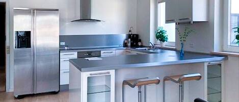 Una cocina moderna con un refrigerador de acero inoxidable, un lavamanos doble y una isla grande con taburetes de bar.