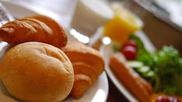 A breakfast plate with croissants, a hot dog, and a side of fruit and vegetables.