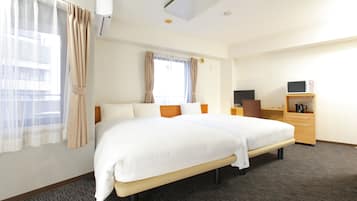 A hotel room with a large bed, a desk with a computer, a coffee maker, and a window with curtains.
