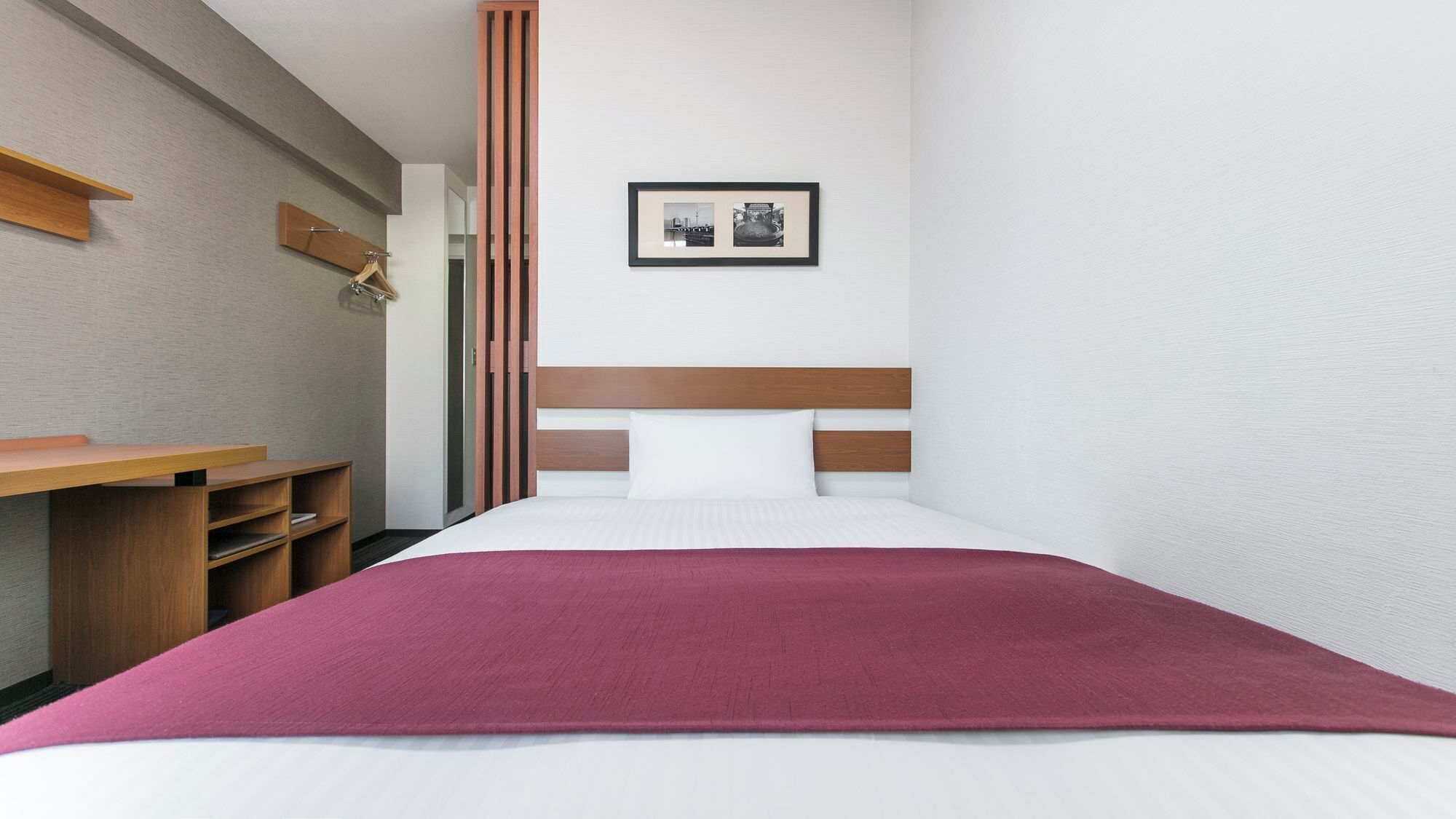 A hotel room with a bed, a desk, and a wall-mounted picture.