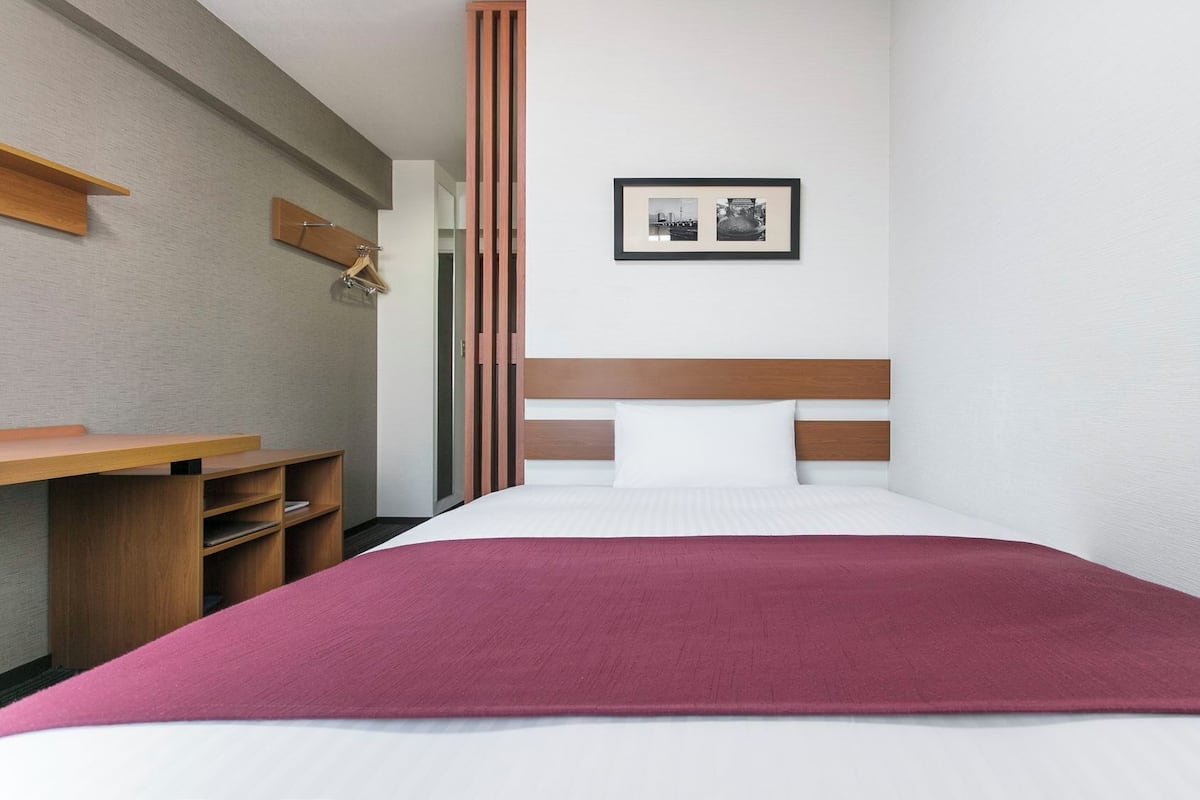 Quarto de hotel com uma cama, uma mesa de trabalho e um quadro na parede.