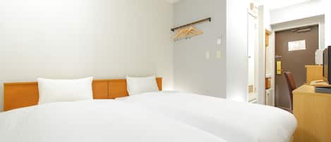 A hotel room with a large bed, a desk with a chair, and a wardrobe.