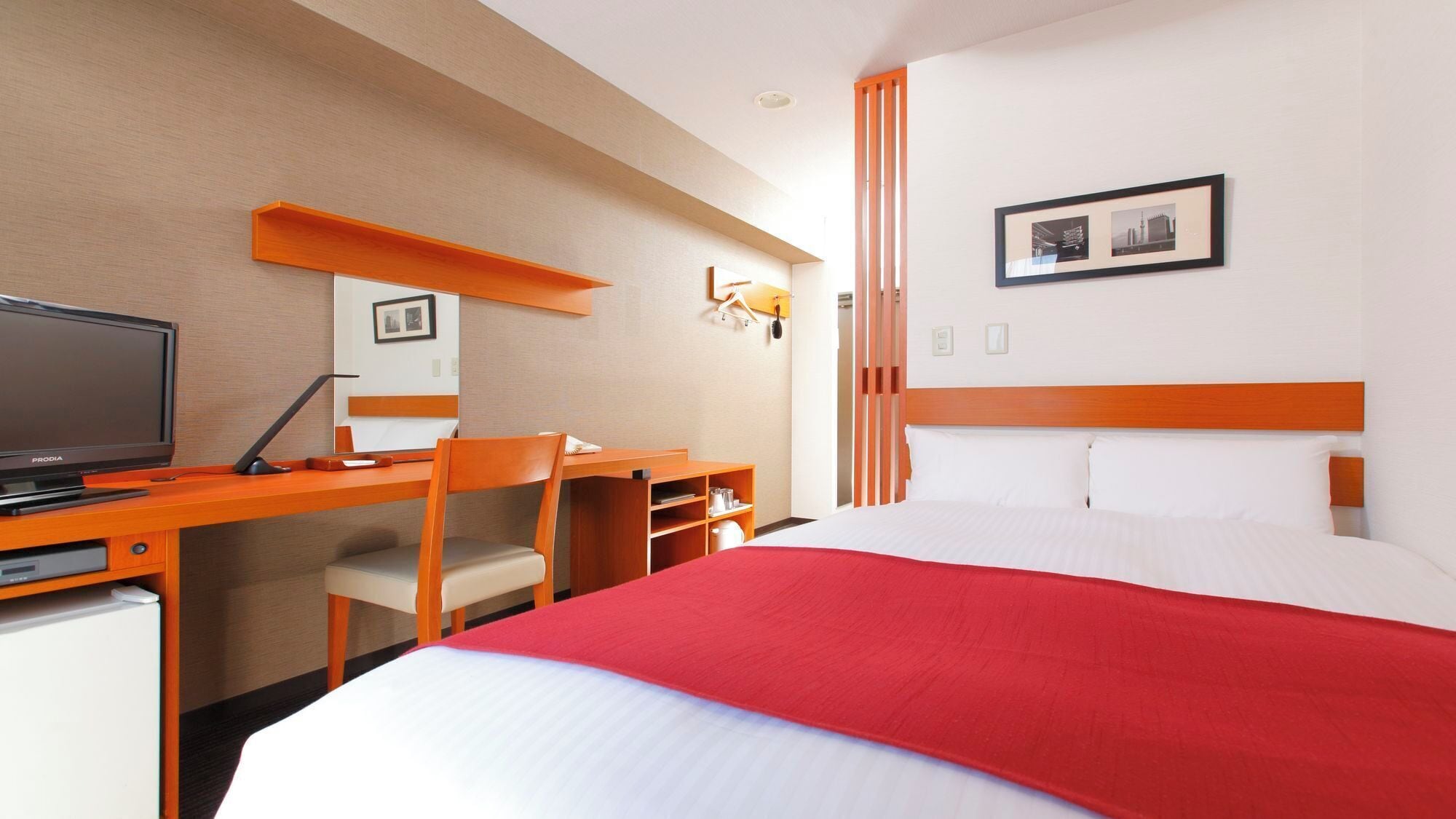 A hotel room with a bed, a desk with a chair, a television, and a wall-mounted picture.
