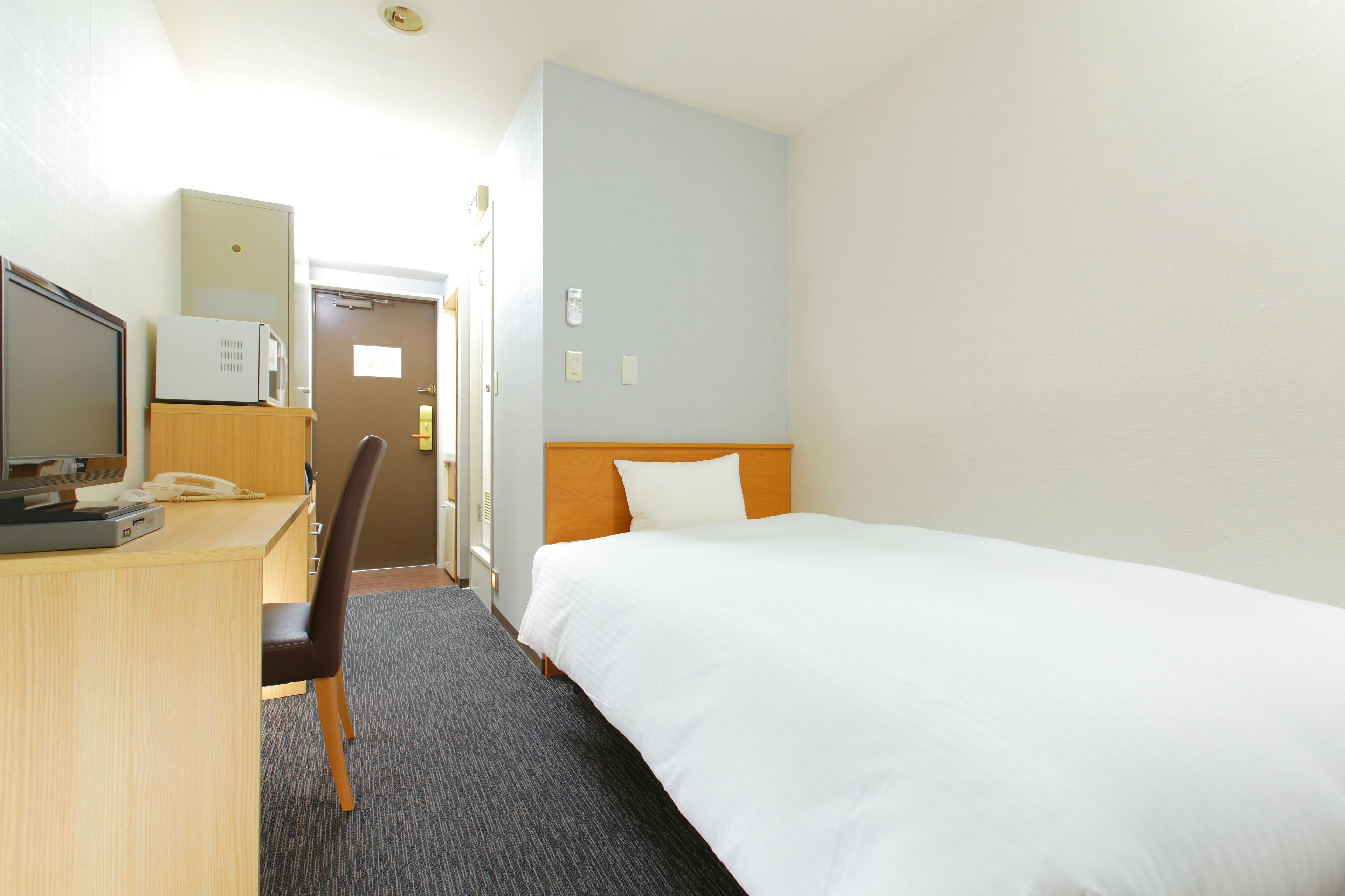 A hotel room with a bed, a desk with a television, a chair, and a door.