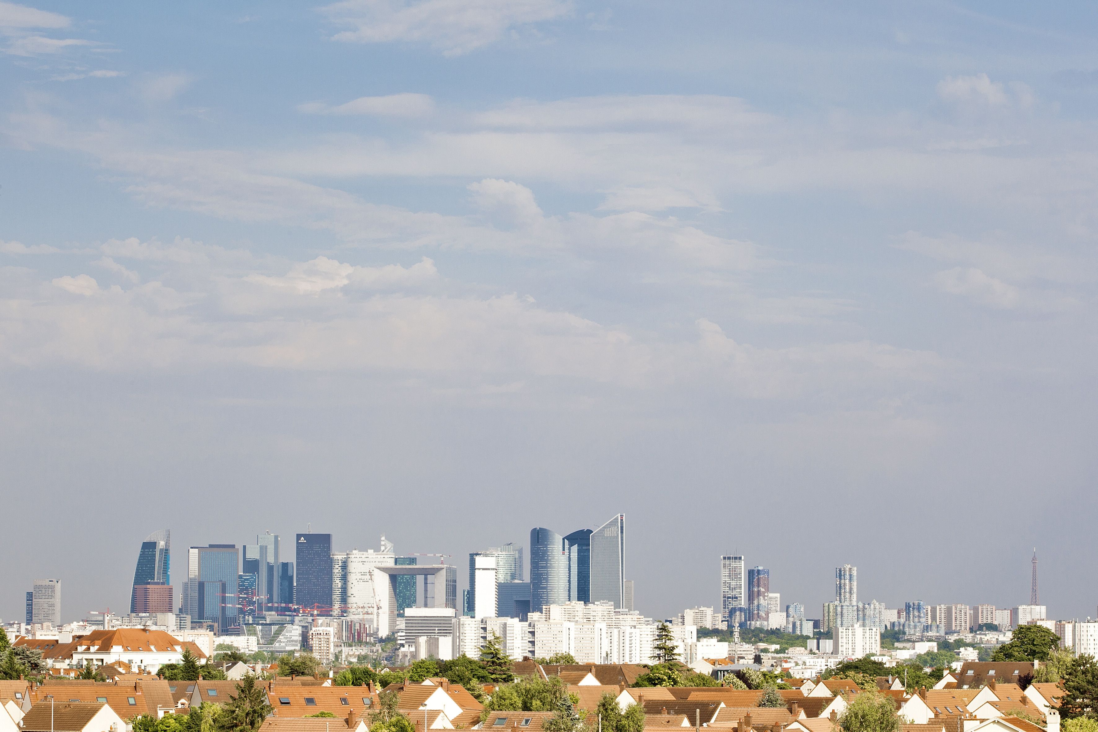 A city skyline with modern high-rise buildings and residential houses with red-tiled roofs.