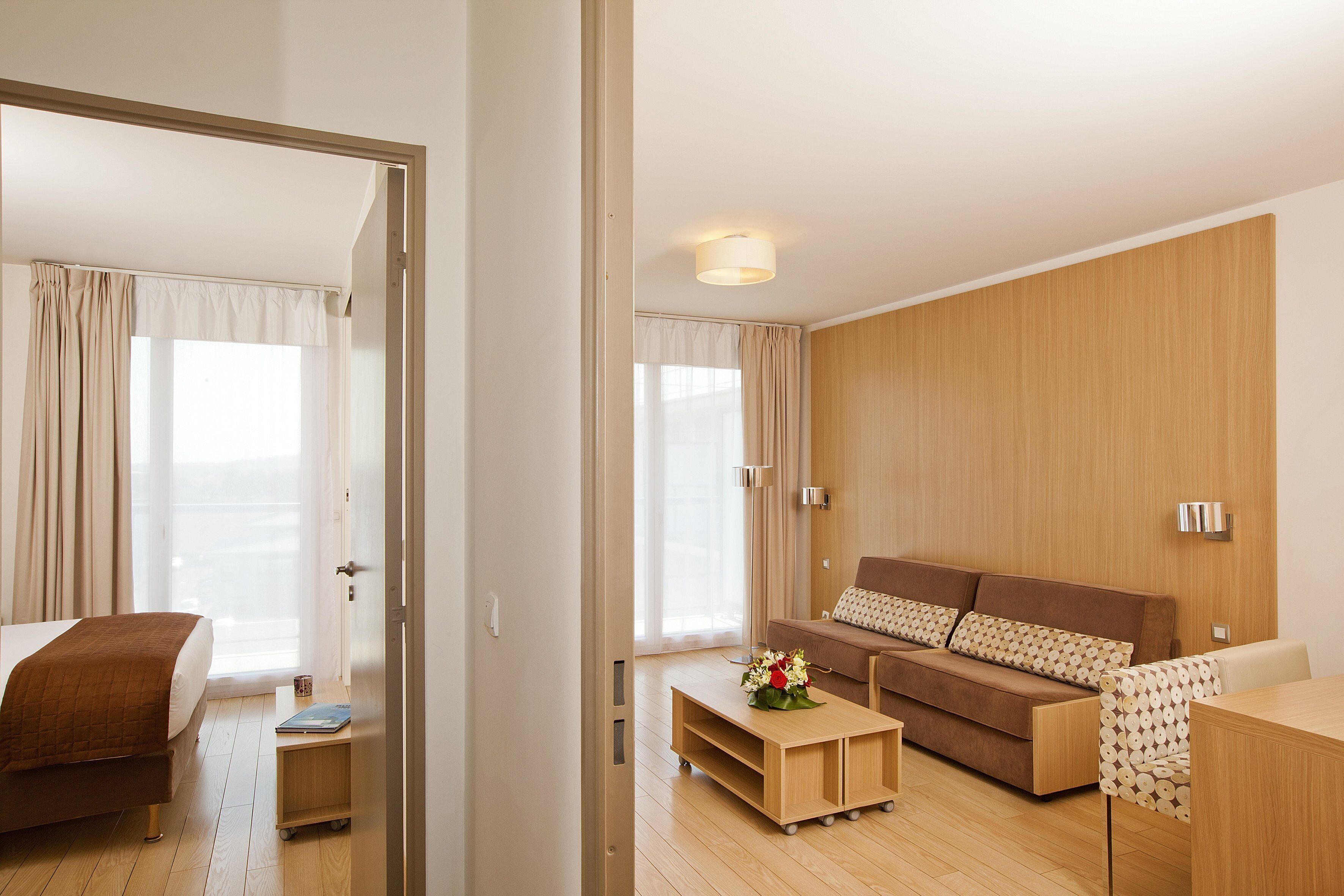 Une chambre d’hôtel moderne, équipée d’un lit, d’un canapé, d’une petite table sur laquelle est posé un vase de fleurs, et d’un panneau mural en bois.