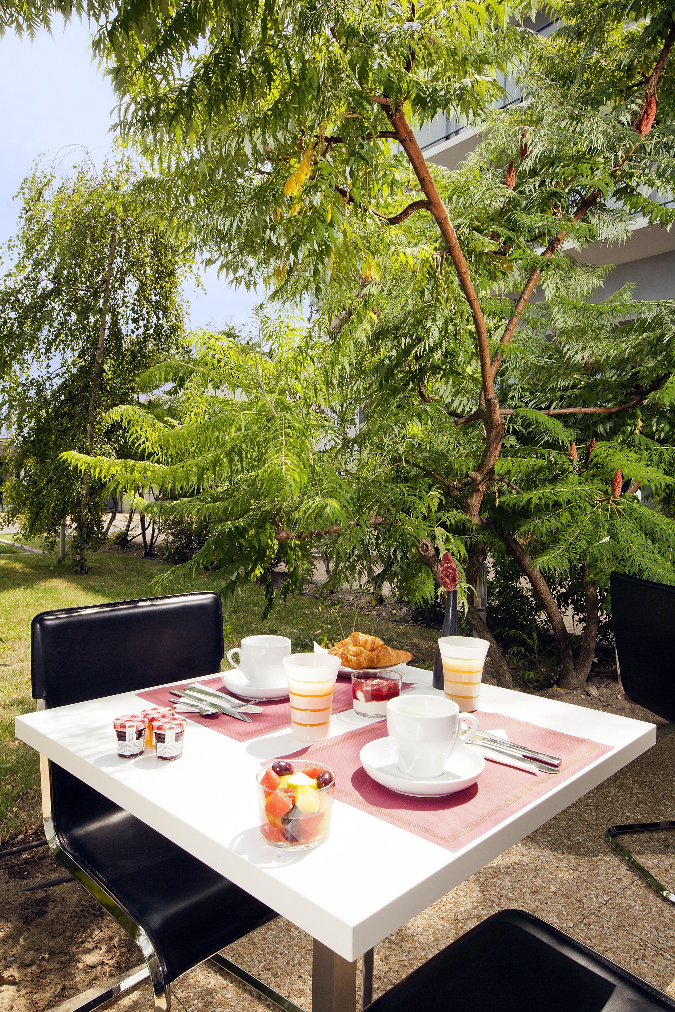 Ein Tisch im Freien, gedeckt mit Frühstücksleckereien, umgeben von üppigem Grün und Bäumen.