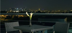 A balcony with a table and chairs, a vase with flowers, and a cityscape view at night. - Residhome Carrières La Défense (Carrieres-sur-Seine)