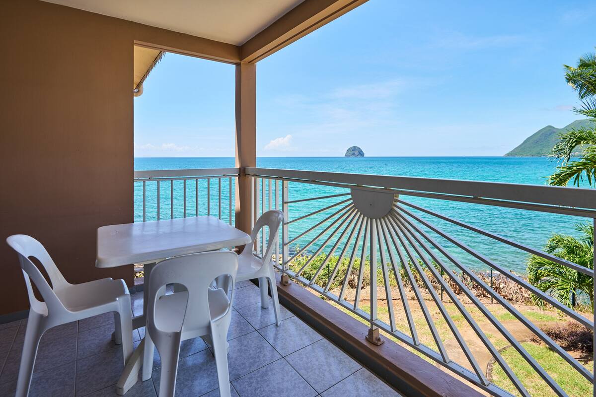 A balcony with a table and chairs, overlooking a turquoise sea and a distant island.