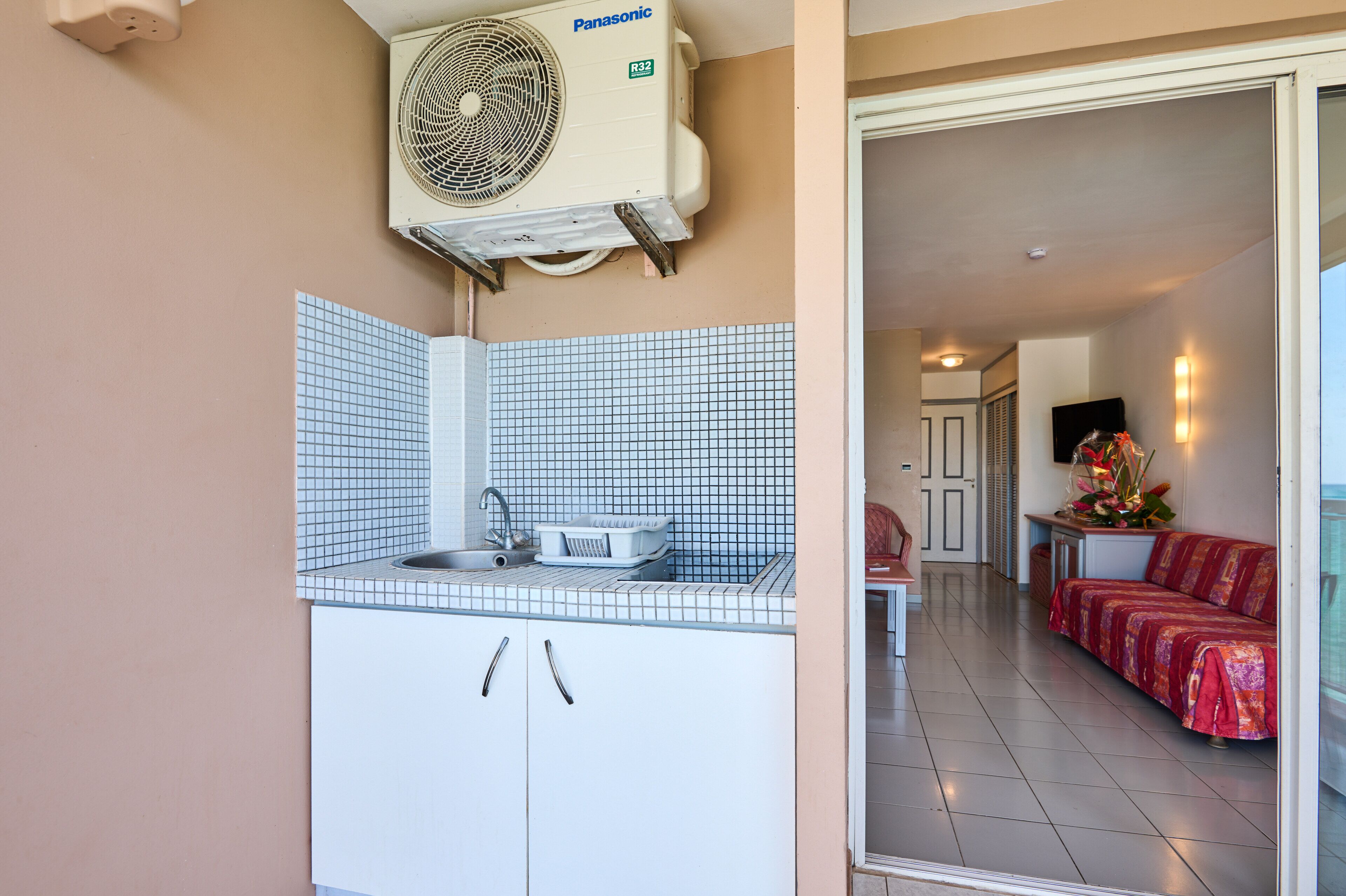 A kitchen with white cabinets, a tiled backsplash, and a Panasonic air conditioner.