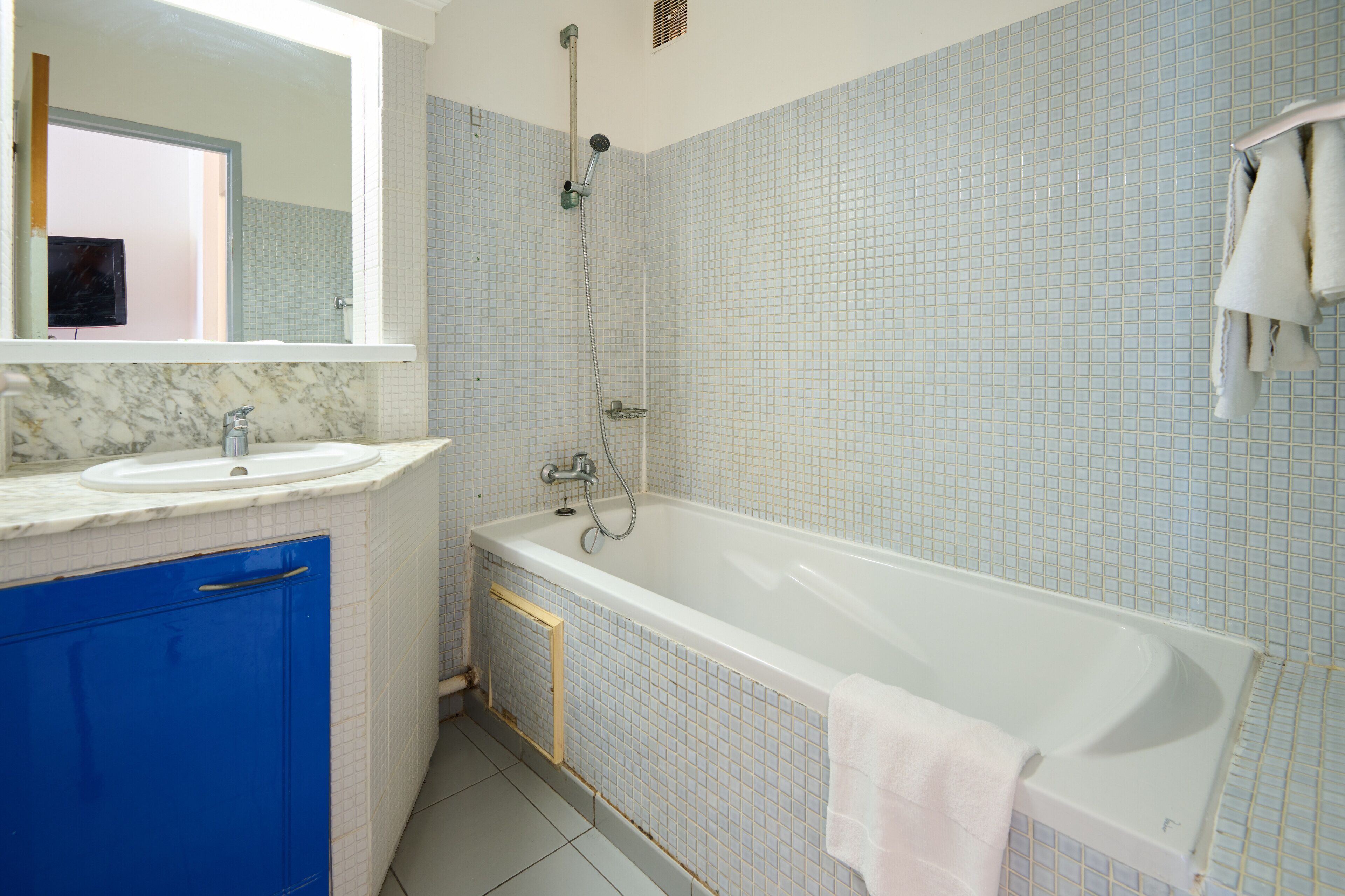 A bathroom with a white bathtub, a blue cabinet, and a white sink.