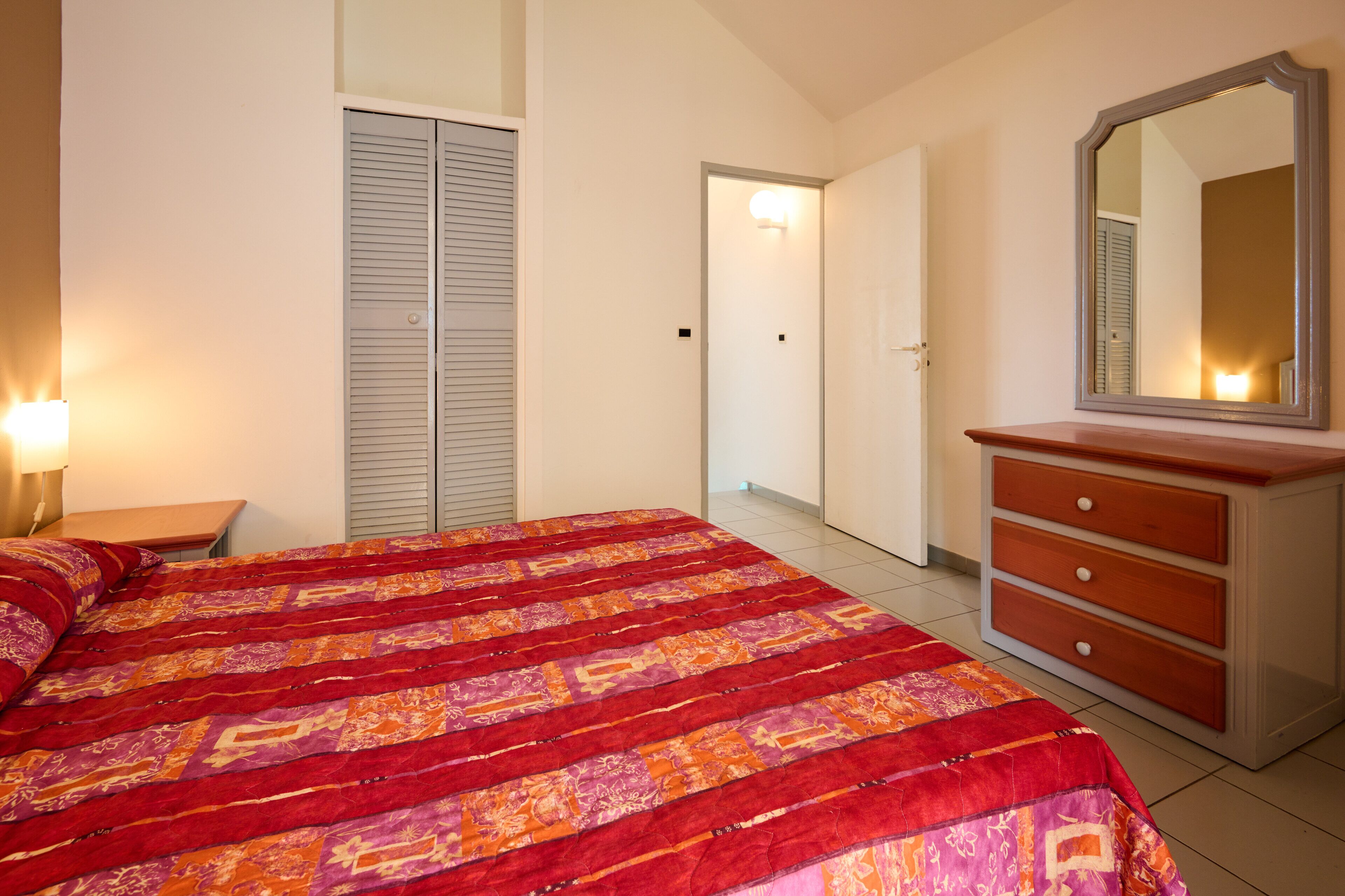 A bedroom with a bed, a dresser, a mirror, and a nightstand.