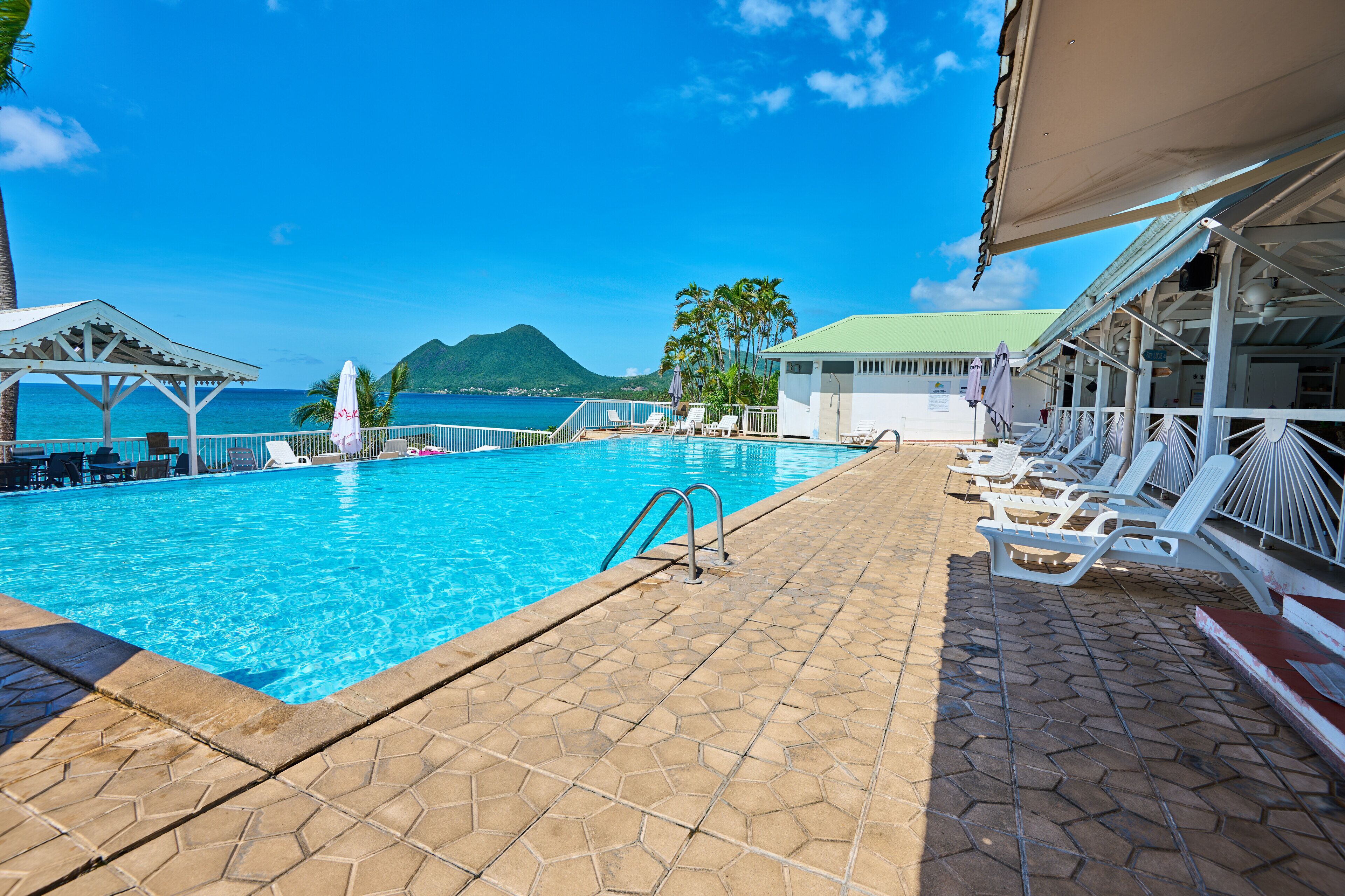 Zona de piscina con vista despejada al océano y una montaña al fondo.