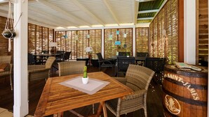 A restaurant with wooden tables and wicker chairs, a cactus centerpiece, and a barrel with 'SAINTS' written on it. - Diamant Beach (Le Diamant)