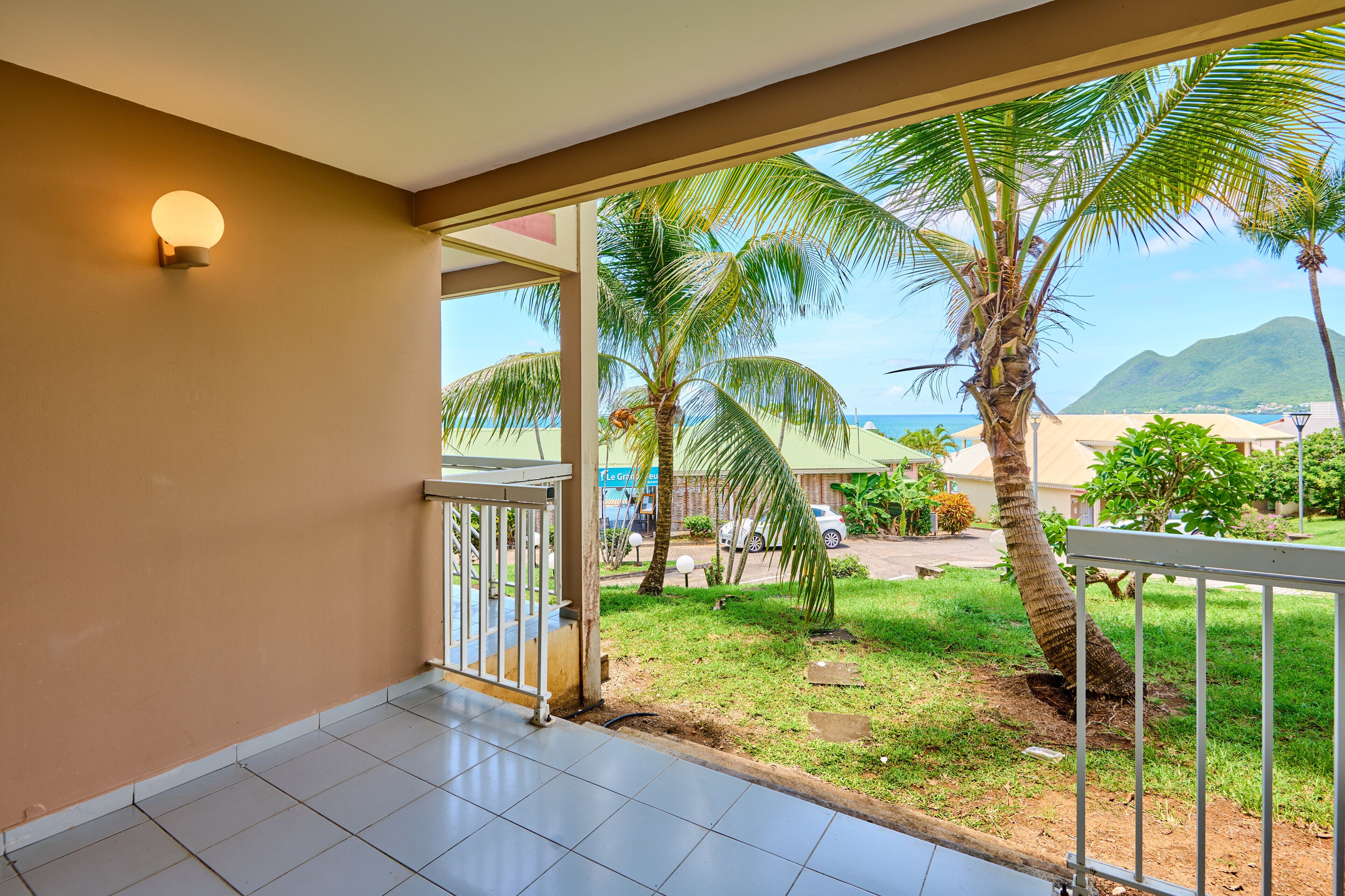 A balcony with a view of a beach, palm trees, and a mountain in the distance.