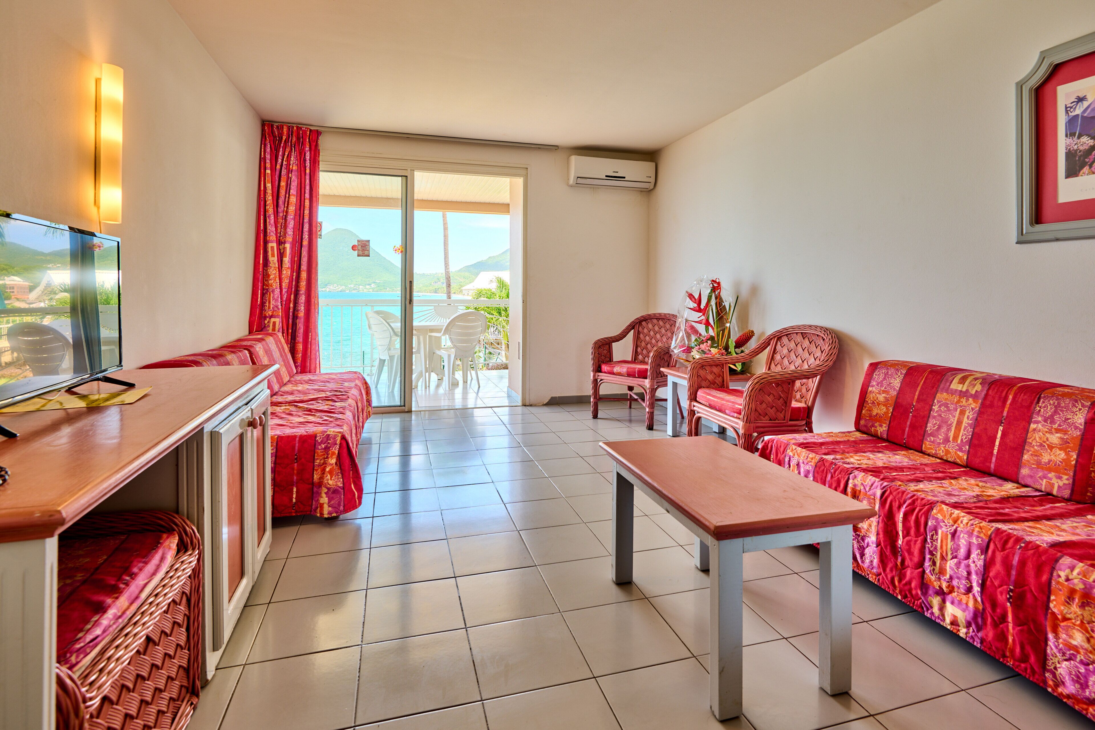 Quarto de hotel com varanda, televisão, sofá, mesa e uma cadeira.