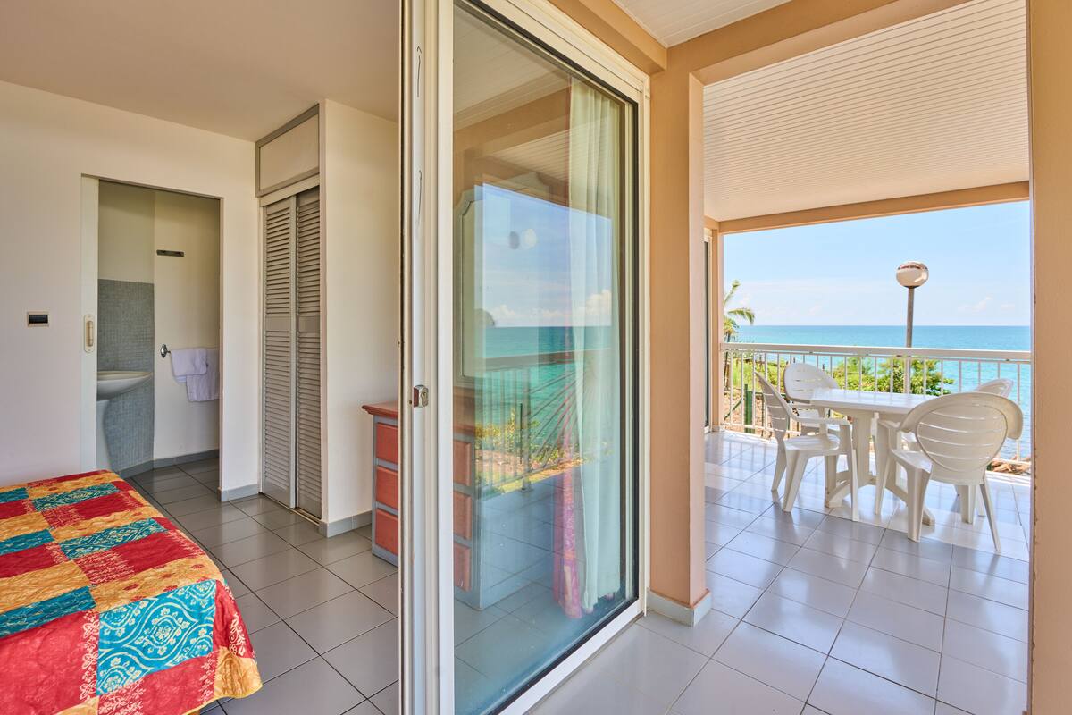 A hotel room with a balcony, a bed, a sliding door, and a view of the ocean.