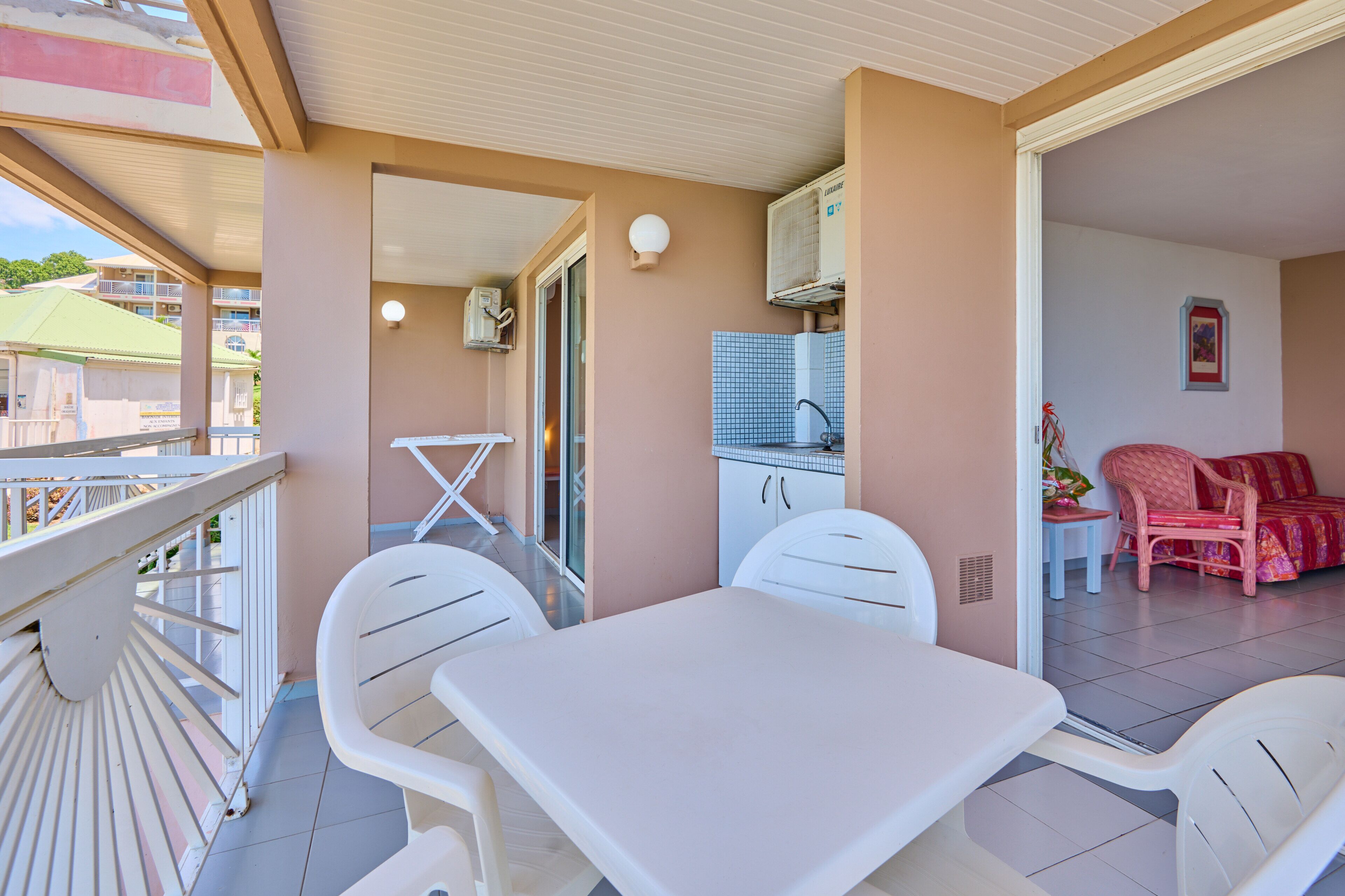 A balcony with a table and chairs, a small kitchen area with cabinets and a sink, and a seating area with chairs and a sofa.