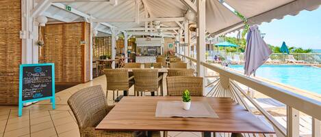 Un espace extérieur aménagé avec des meubles en osier, une table en bois et une vue sur une piscine.
